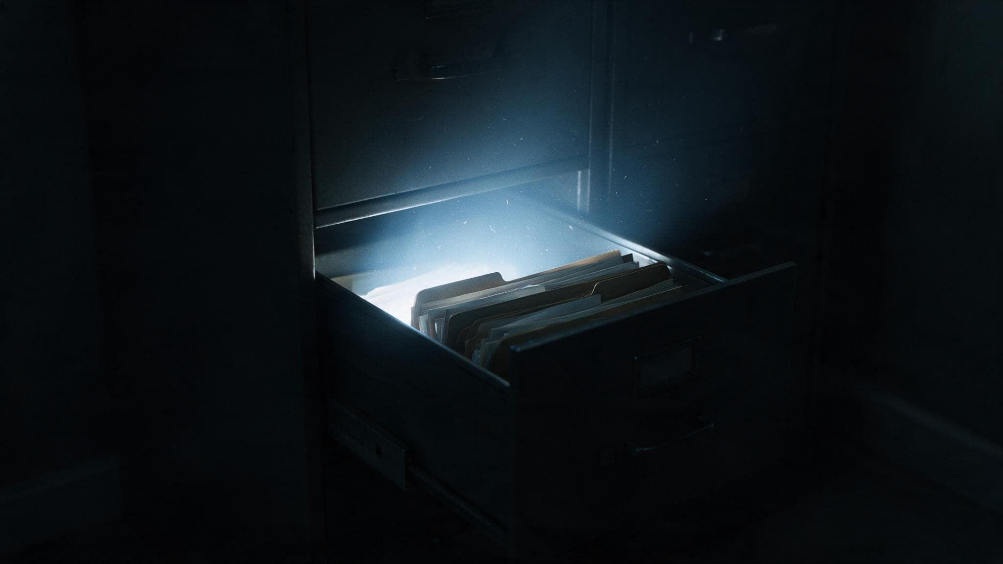 A filing cabinet drawer standing open in a dark room with light pouring out of it