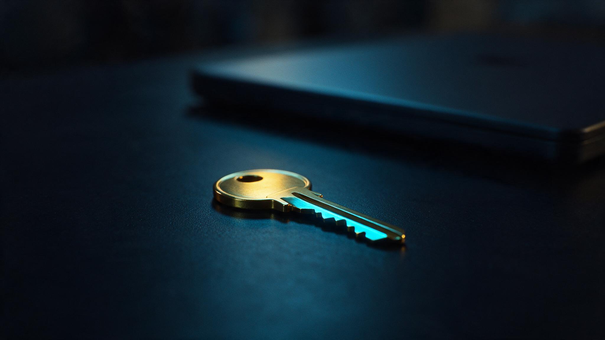 A single brass door key on a dark desk beside a closed laptop